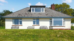 Ein zweistöckiges Haus mit geneigtem Dach, einem Schornstein und einer kleinen Veranda mit zwei Bänken.