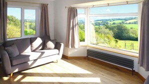 Ein Zimmer mit einer Couch, einer Heizung und großen Fenstern mit Blick auf eine grüne Landschaft.