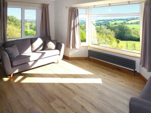 Une pièce comprenant un canapé, un radiateur et de grandes fenêtres donnant sur un paysage verdoyant.