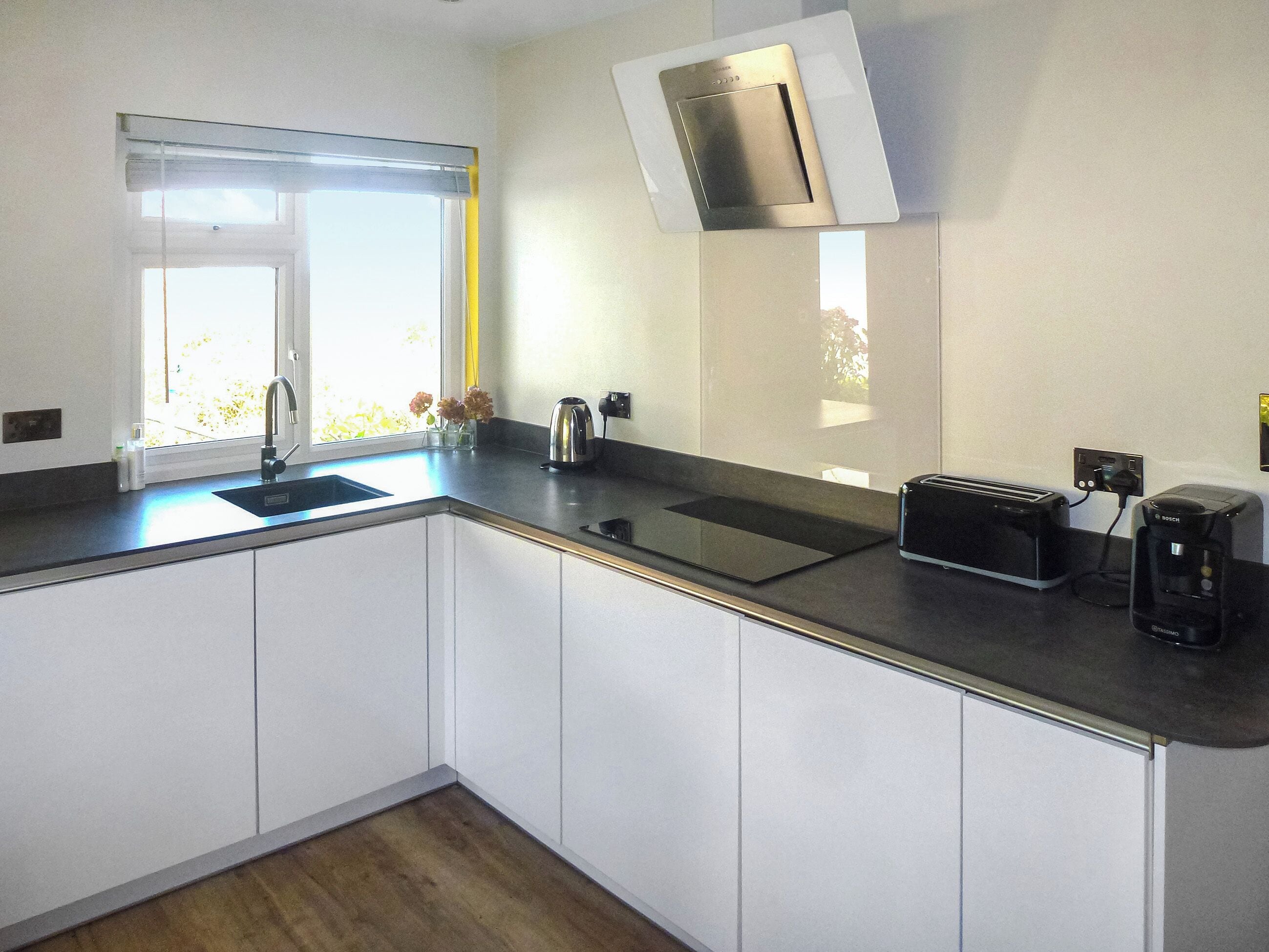 A modern kitchen with a sink, a toaster, a coffee maker, and a window with a view of greenery.