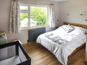 A bedroom with a bed, a window with curtains, a radiator, and a wooden floor. - 3 bedroom accommodation in Whitestone (Whitestone)