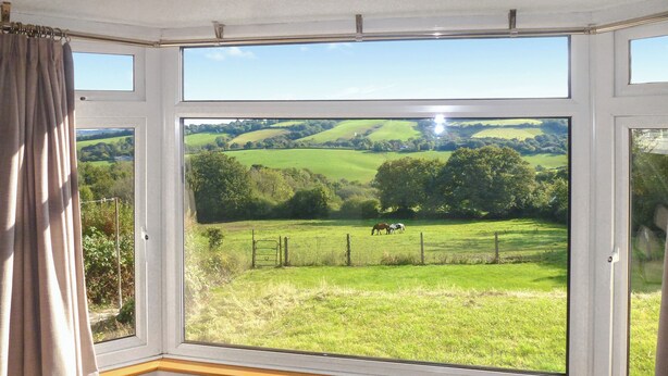 Ein Zimmer mit großem Fenster mit Blick auf ein grünes Feld und Pferde.