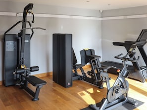 Ein Fitnessstudio mit Trainingsgeräten, darunter eine Bank, ein Krafttrainer und ein Crosstrainer.
