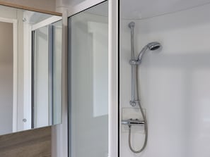 Ein modernes Badezimmer mit Duschkabine aus Glas, einer Handbrause und einer wandmontierten Bedienung.