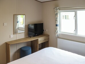 A hotel room with a bed, a TV on a wooden desk, a mirror, a window with curtains, and a radiator. - Keswick 17 - UK51391 (Narberth)