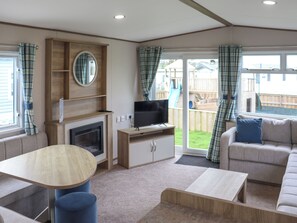 A living room with a fireplace, television, sofa, and a dining table. - Keswick 17 - UK51391 (Narberth)