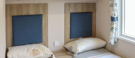 A bedroom with two beds, wooden headboards, a small shelf, and a window with curtains.
