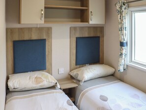 A bedroom with two beds, wooden headboards, a small shelf, and a window with curtains.