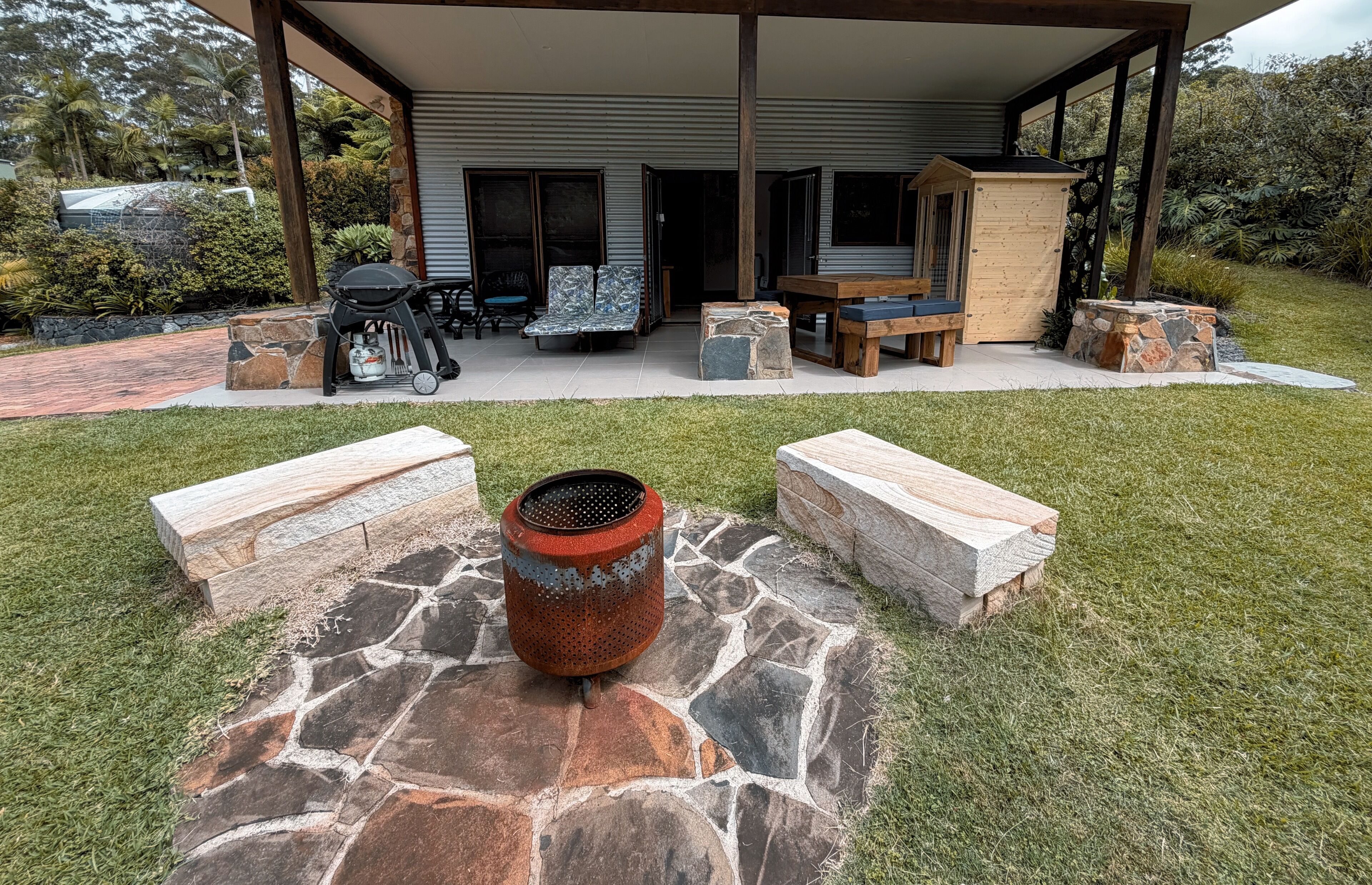 A covered outdoor seating area with stone planters, a grill, and a wooden table.
