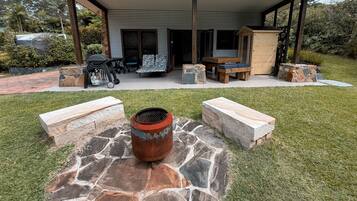 A covered outdoor seating area with stone planters, a grill, and a wooden table.