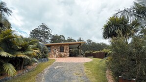 A stone house with a covered patio, surrounded by lush greenery and a gravel driveway. - Cabin One- Sauna, pet-friendly, adults only (Lowanna)