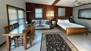 A room with a wooden dining table, two wooden chairs, a sofa, a bed, and a ceiling fan. - Cabin One- Sauna, pet-friendly, adults only (Lowanna)