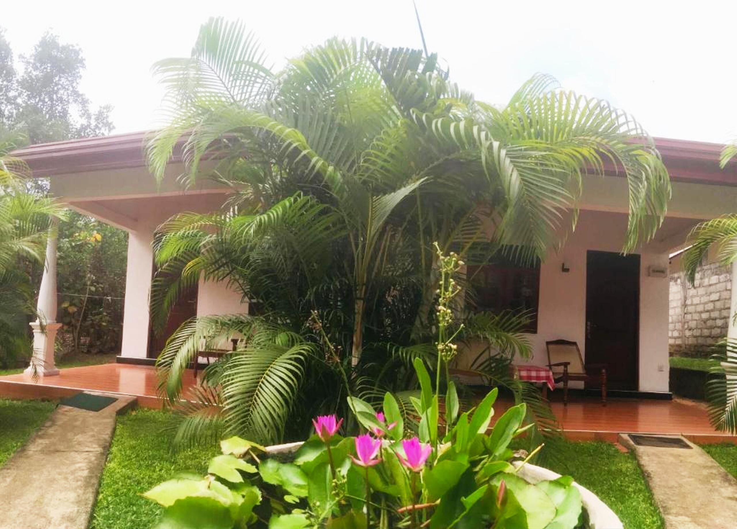 A covered outdoor area with a garden, a pathway, and a building with a red roof.