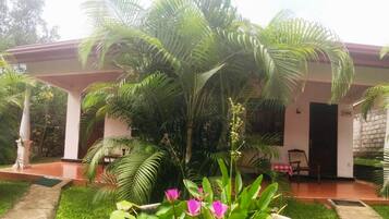 A covered outdoor area with a garden, a pathway, and a building with a red roof.
