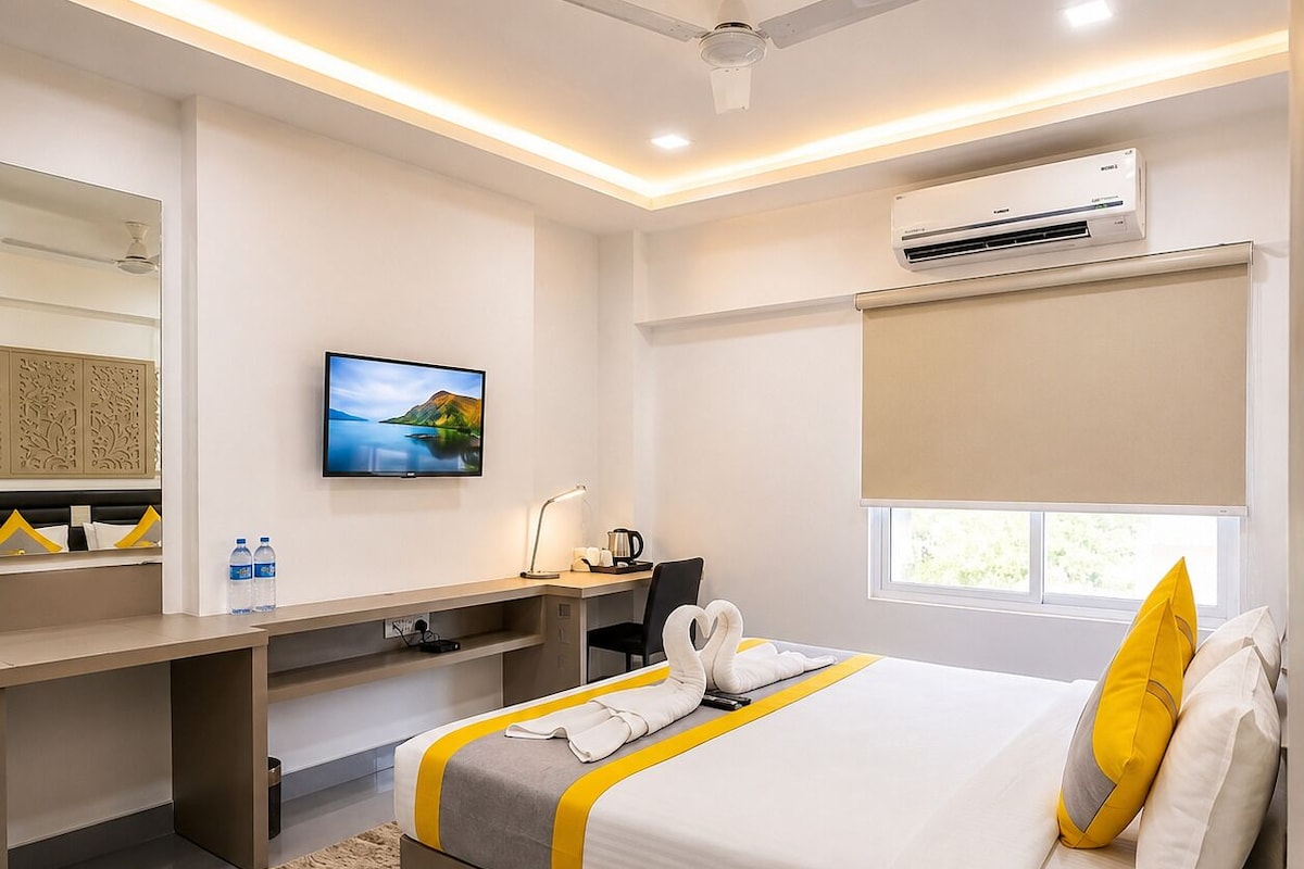 Quarto de hotel com cama, escrivaninha, cadeira, televisão, aparelho de ar condicionado e janela.