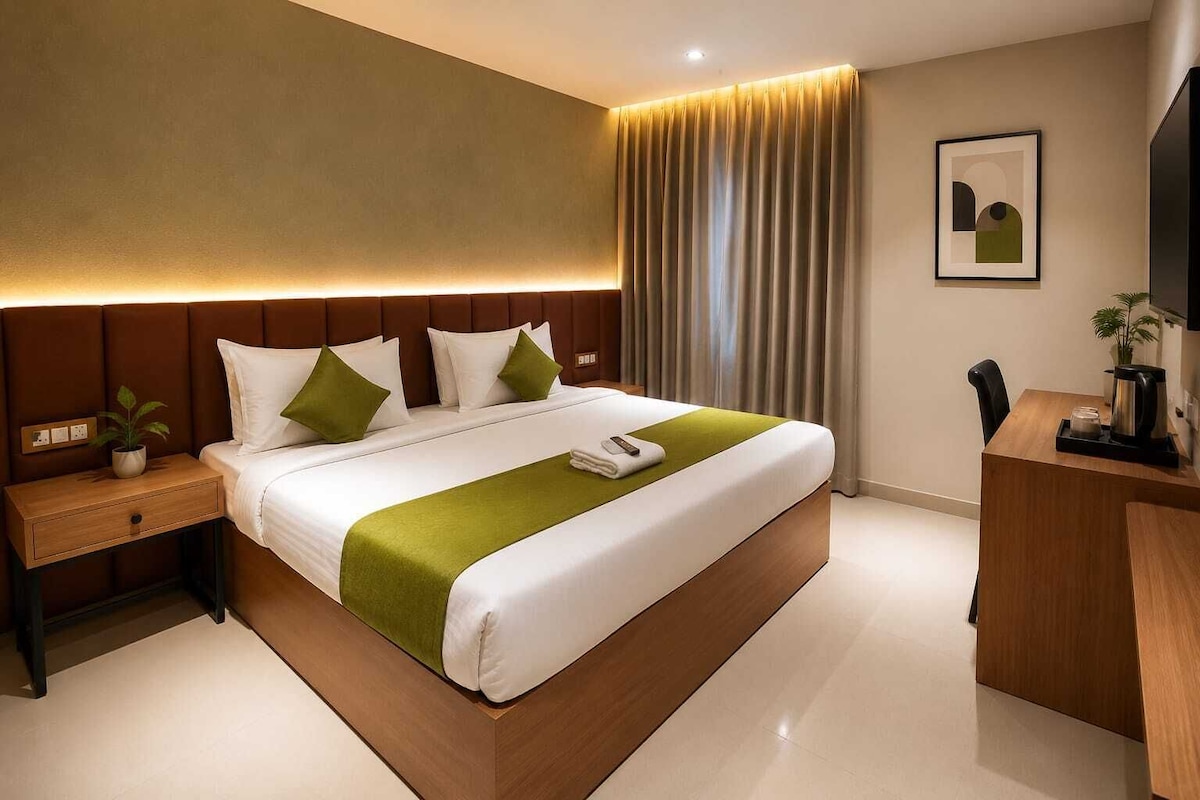 Quarto de hotel moderno com uma cama grande, uma mesinha de cabeceira, uma escrivaninha e uma cadeira.
