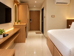 Une chambre d’hôtel moderne, équipée d’un lit, d’une télévision, d’un bureau avec une plante et d’une porte donnant sur une autre pièce.