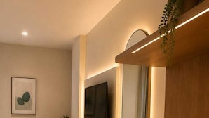 A modern living room with a wooden console, a flat-screen TV mounted on the wall, and a comfortable seating area with a sofa and a chair. - La Riviera Suites (Hyderabad)