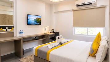 Quarto de hotel com cama, escrivaninha e ar condicionado.