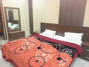Habitación de hotel con cama, mesita de noche, cómoda, espejo y botella de agua.