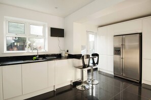 A modern kitchen with white cabinets, a stainless steel refrigerator, and two black bar stools. - Private Double Room ensuite in Cheshunt nr London (Cheshunt)