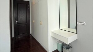 Un pasillo con suelo de madera oscura, paredes blancas, un espejo grande y una consola blanca.