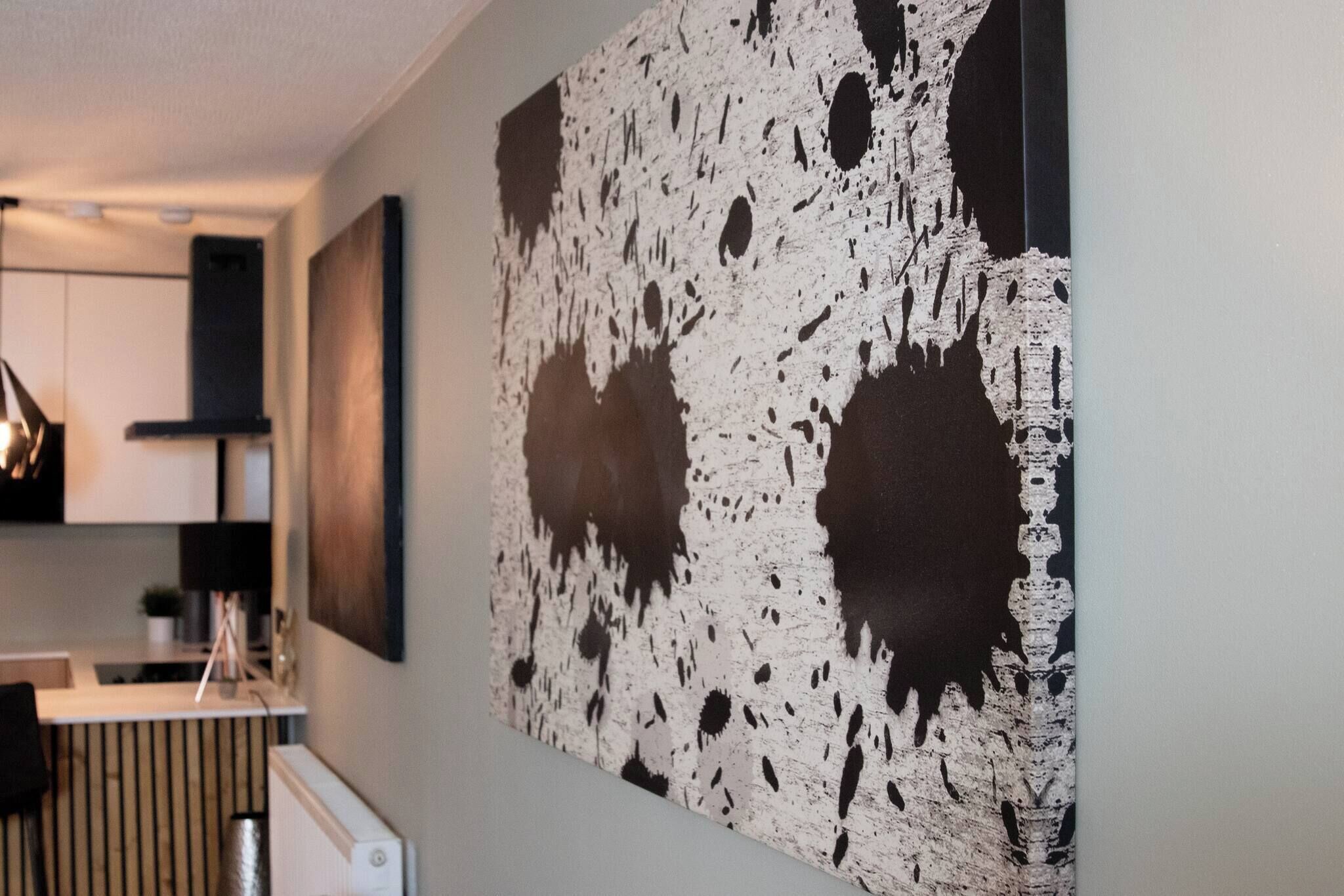 A modern kitchen with white cabinets, a black countertop, and a large abstract painting on the wall.