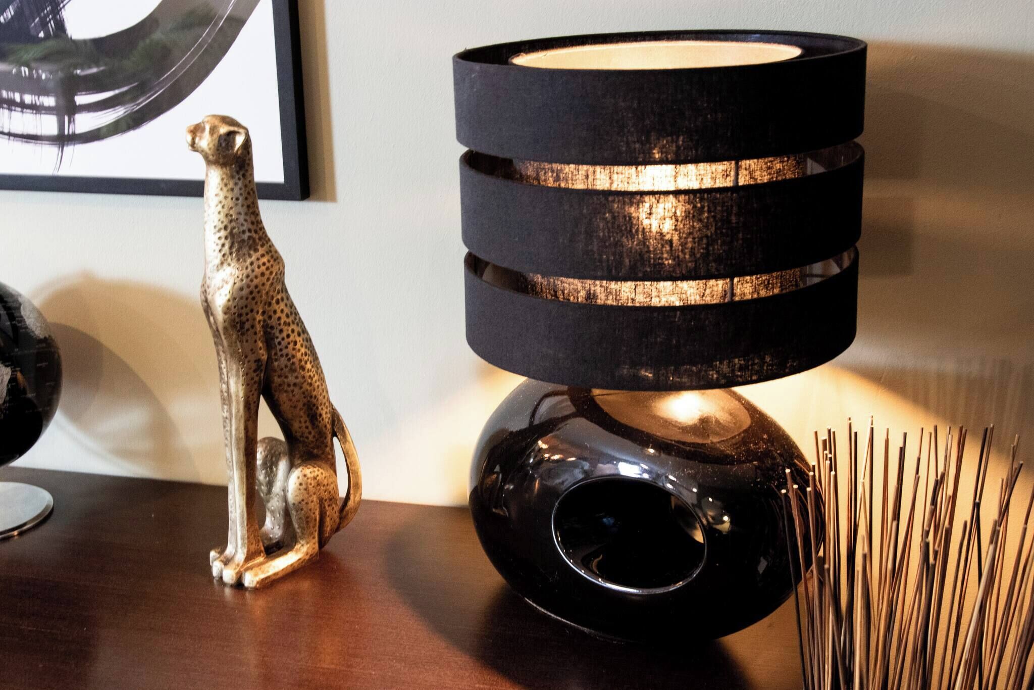 A table with a black lamp, a decorative animal figurine, and a vase with sticks.