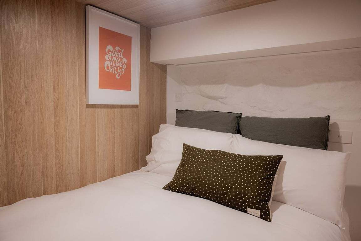A neatly made bed with white and dark pillows, a framed artwork on the wall, and a wooden panel on the left.