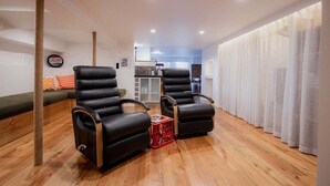 A modern living room with two black leather recliners, a wooden floor, a small red side table, and a view into the kitchen area. - The Funky Den on Warwick (Hobart City)