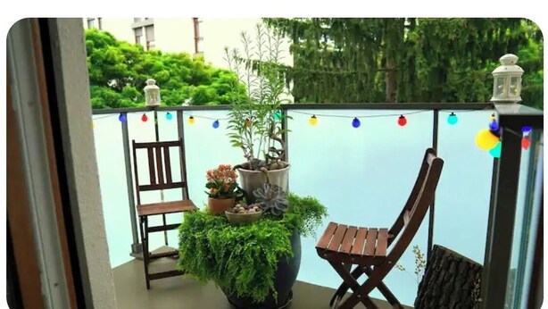 A balcony with a wooden chair, a potted plant, and a string of colorful lights. - Room in a Stunning Apartment in the City and the Countryside (Oullins-Pierre-Bénite)