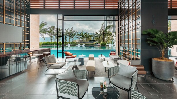 Una moderna zona relax all'aperto con piscina, arredi e vista su palme e edifici.