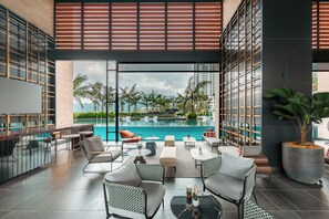 Un espace de détente extérieur moderne, doté d’une piscine, de sièges et offrant une vue sur les palmiers et les bâtiments.