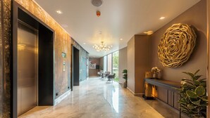 Una hall moderna di un hotel, con pavimento in marmo, ascensori, una reception e un'ampia opera d'arte astratta a parete.