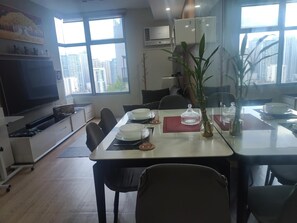 A dining area with a table set for four, a television, and a city view through large windows. - [KStayB]2BR+2Bath+Livingroom/Wellness & Clean Stay (Makati City)