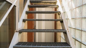 Eine schmale Treppe mit Metallgeländern und einem Metallgitter am unteren Ende, die zu einer Tür führt.