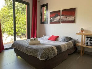 A bedroom with a bed, a nightstand, a lamp, and two paintings on the wall. - Les Hauts de la Testa (Sainte-Lucie de Porto-Vecchio)