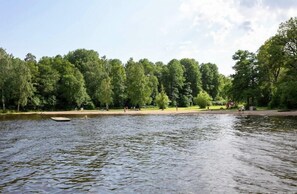 A calm lake with a wooden dock, surrounded by dense green trees and a clear sky. - Nordic Camping Västerås Mälarcamping (Vasteras)