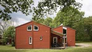 Une cabane en bois à deux étages, dotée d’un porche et d’une petite terrasse, entourée d’une végétation luxuriante.