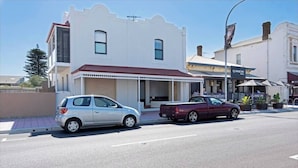 A street view with a white building with a red roof, a parked silver car, and a maroon pickup truck.