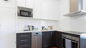 A modern kitchen with white cabinets, a stainless steel dishwasher, a microwave, a stove, and a clock on the wall.
