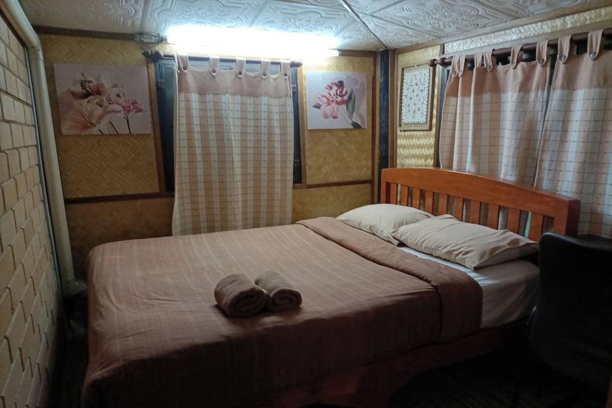 Un lit simple avec une tête de lit en bois, deux oreillers et deux serviettes enroulées posées sur le lit.