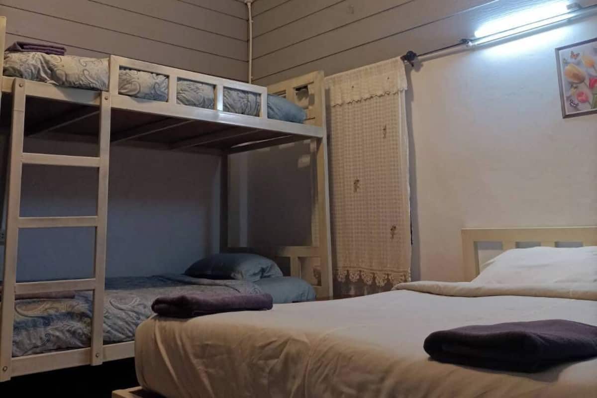 Une chambre de type dortoir, avec des lits superposés, un ventilateur de plafond et un luminaire fixé au mur.