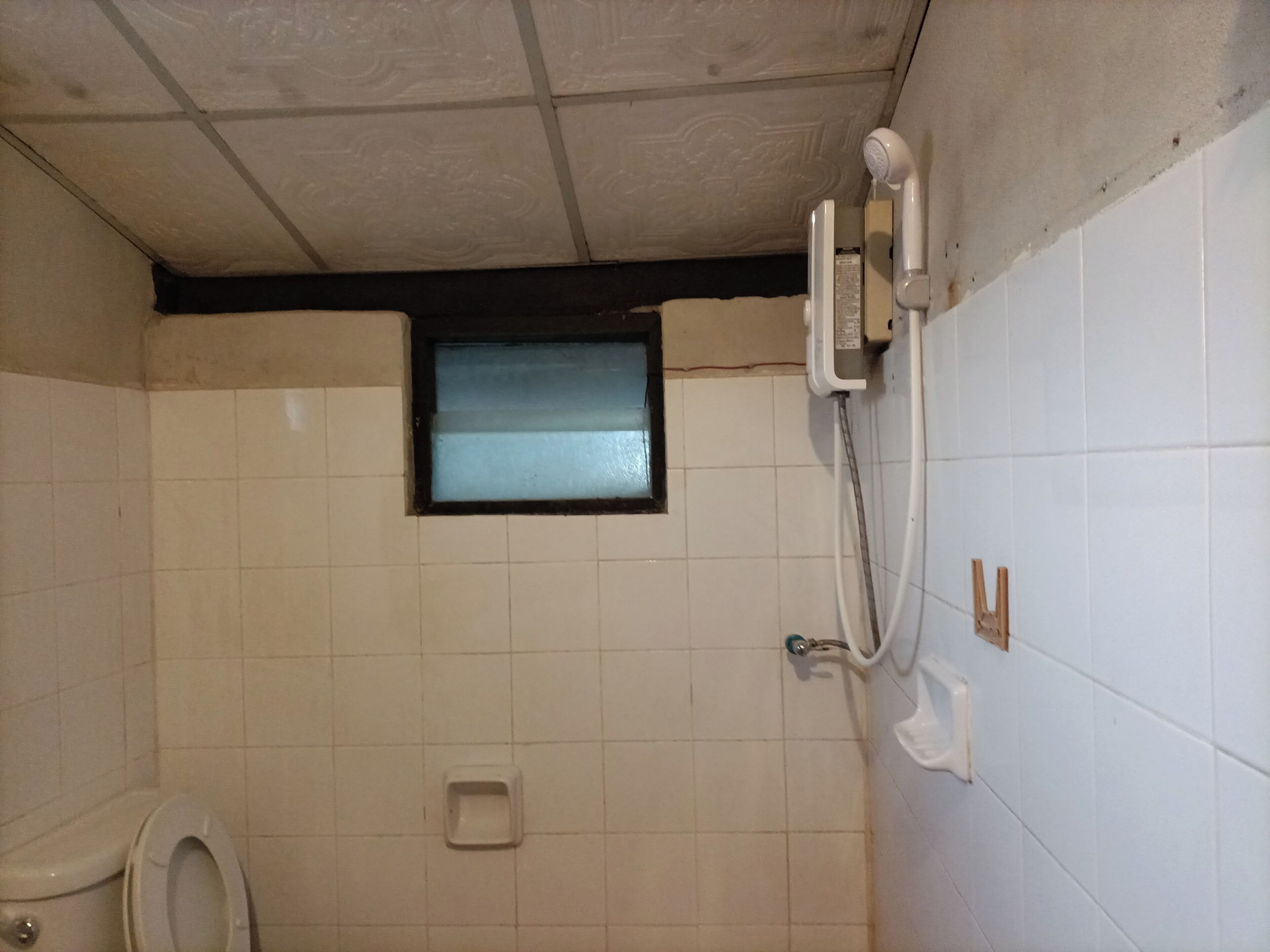 A small, tiled bathroom with a toilet, a window, and a shower.