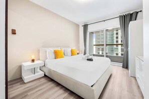 A modern hotel room with a large bed, a bedside table with a lamp, a wardrobe, and a view of the city through a large window. - StayShort - Chic 1BR Retreat in Dubai Marina that Sleeps 4 (Dubai Marina)