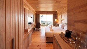A wooden interior with a bed, bedside table, lamp, and a view of the outdoors.