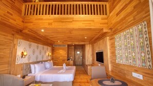 A wooden cabin room with two beds, a TV, a dining table with fruit, and a patterned wall.