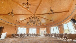 A spacious conference room with wooden paneling, multiple chandeliers, and large windows offering a view of the outdoors.