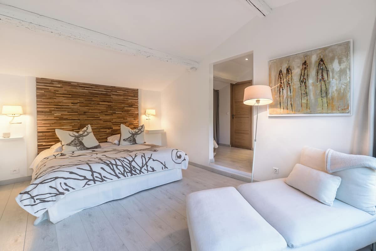 A modern bedroom with a wooden headboard, a large bed with a tree branch design, two bedside lamps, and a painting on the wall.