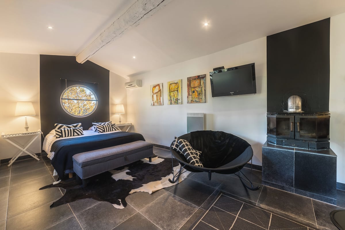 A modern bedroom with a bed, a chair, a fireplace, and artwork on the wall.